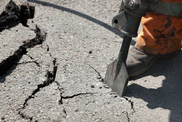 Entsiegelung (Foto: sima / stock.adobe.com= Eine Person, die mit einem Schlagbohrer Asphalt knackt und dadurch eine Fläche entsiegelt.