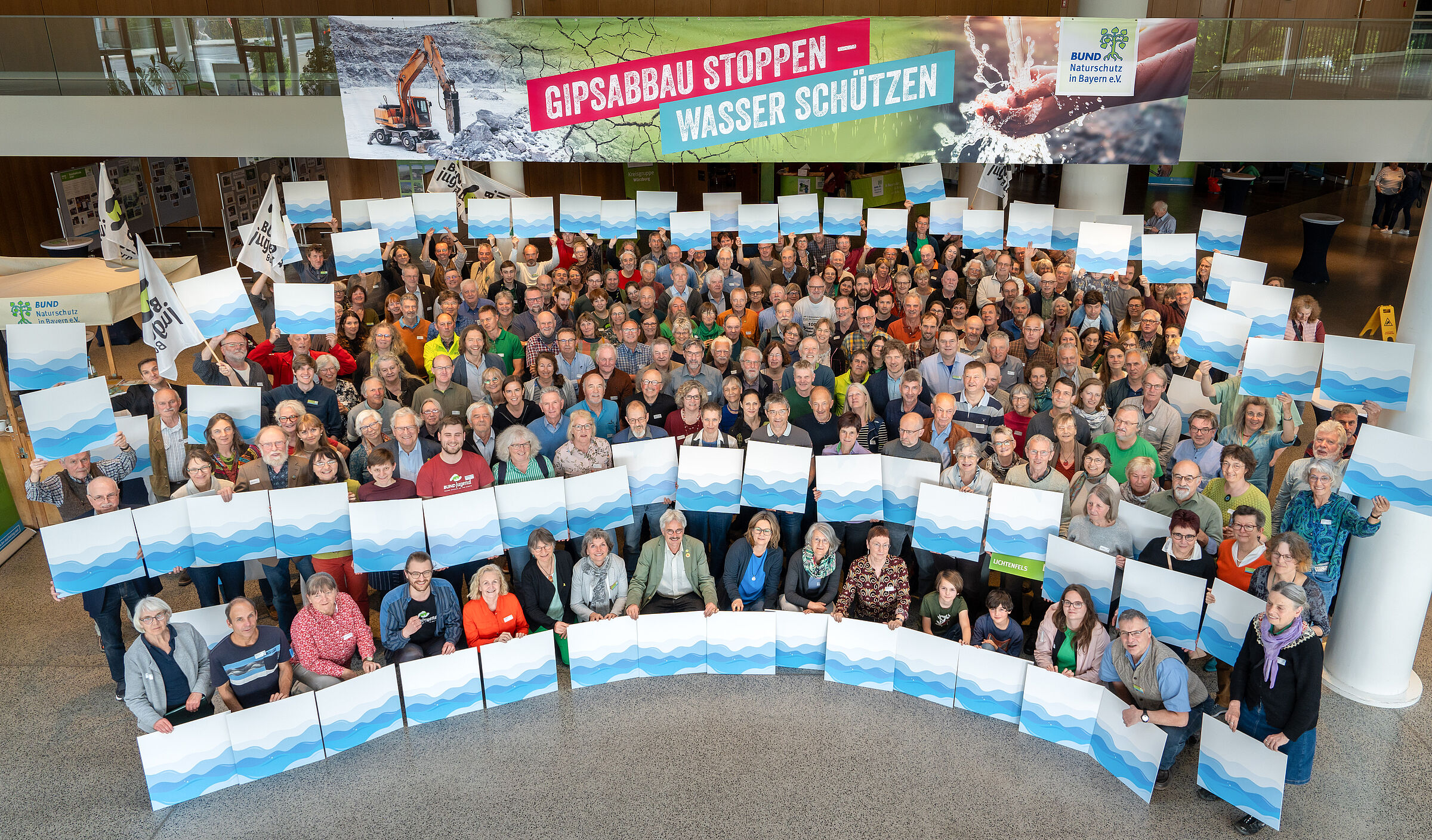 Die Delegierten des BUND Naturschutz stehen in einer großen Gruppe beieinander und halten Schilder mit symbolischen Wellen, um für mehr Wasserschutz zu demonstrieren.