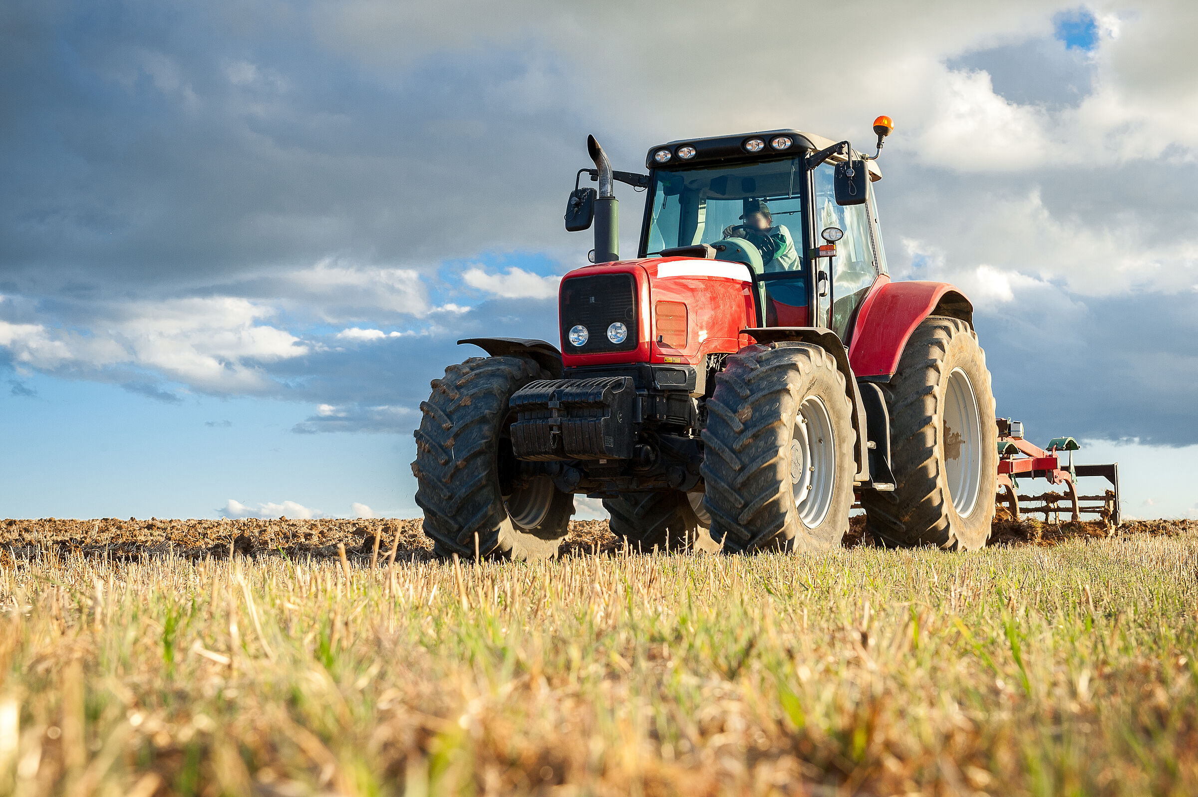 Disounter-Bio: Ein roter Traktor fährt auf dem Feld, über ihm wolkiger Himmel