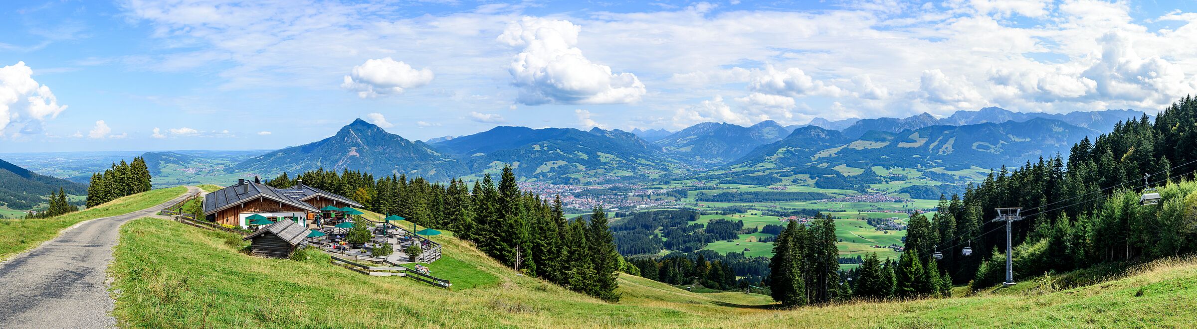 Problem der Almwirtschaft: Ein asphaltierter Weg im sommerlichen Oberallgäu, im Hintergrund eine Skihütte sowie ein Lift