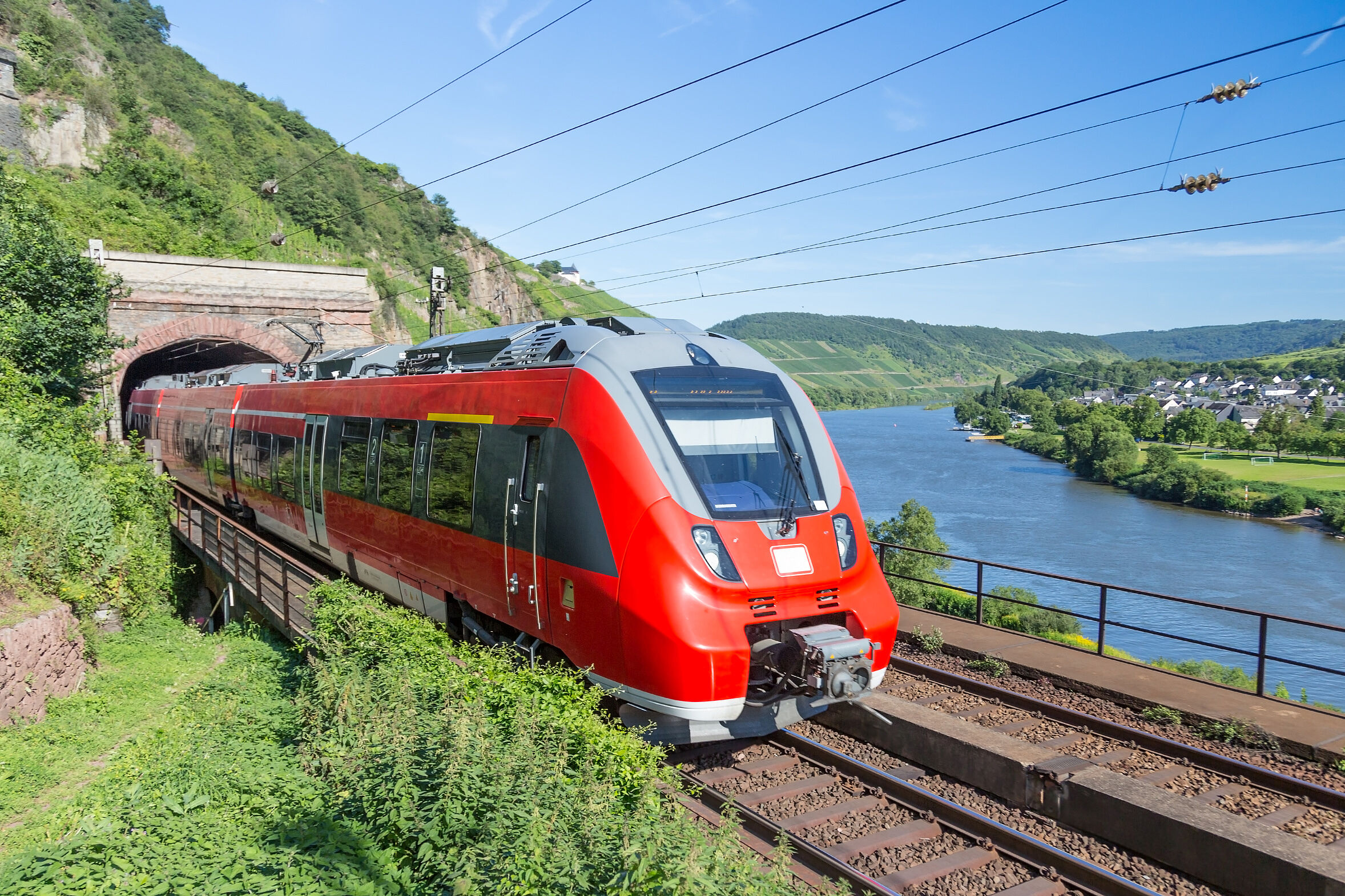 Eine Regionalbahn fährt aus einem Tunnel, im Hintergrund ein Flusslauf: Energiewende und Herausforderungen für den Verkehrssektor ergänzen sich, für mehr Effizienz und Umstieg auf Erneuerbare Energien muss der elektrifizierte Schienenverkehr ausgebaut werden. (Foto: Kruwt/AdobeStock)