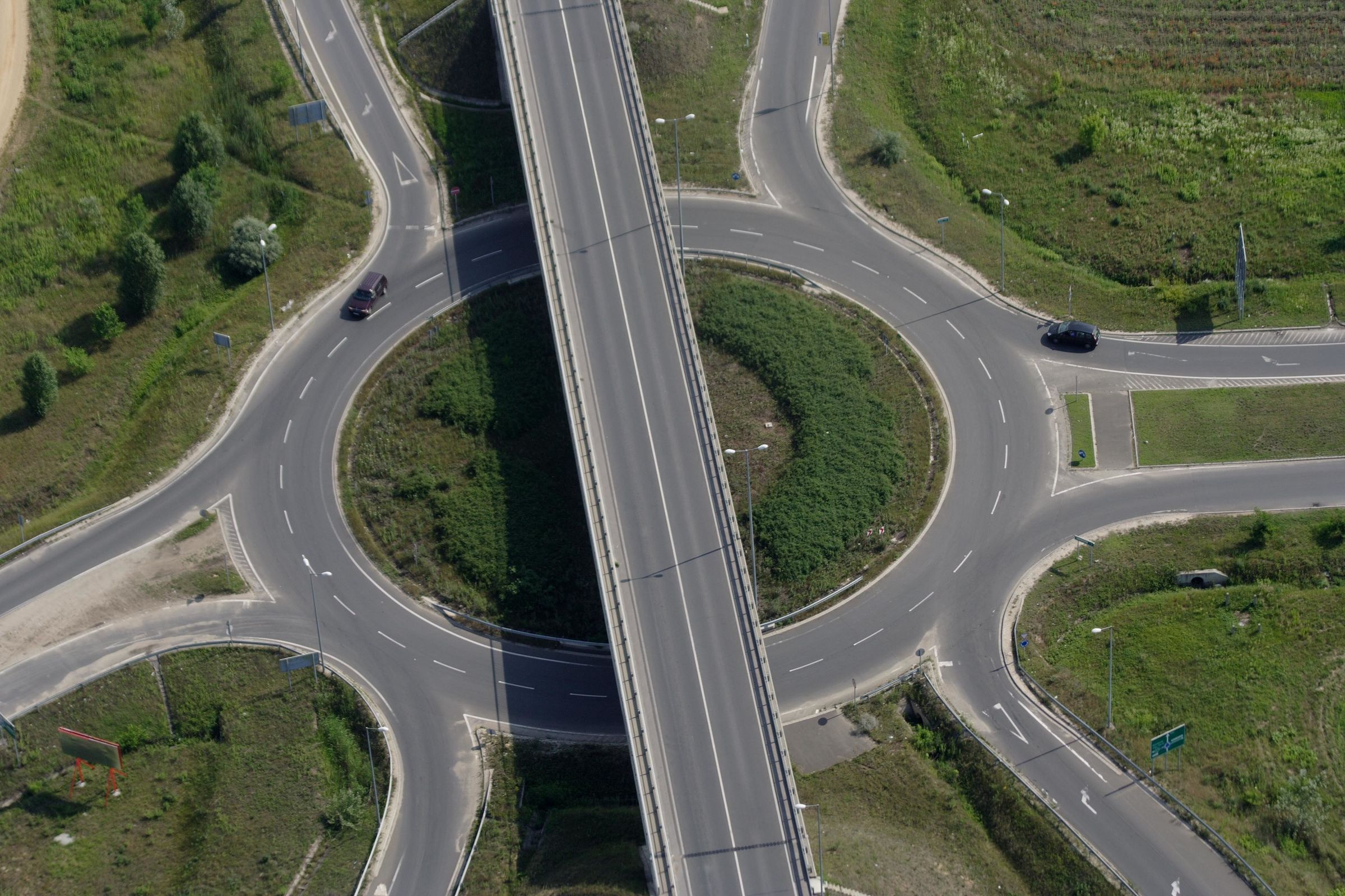 Luftaufnahme eines Kreisverkehrs mit sechs Abzweigen: Der Straßenverkehr muss jetzt die richtige Ausfahrt nehmen, damit Flächenverbrauch und die zahlreichen negativen Auswirkungen verringert werden. (Bild: oroszgy/AdobeStock) 