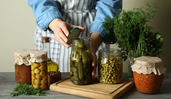 Lebensmittel konservieren: Ein typisches eingelegtes Gemüse sind saure Gurken. (Foto: Atlas/stock.adobe.com) Lebensmittel konservieren: Eine Frau schließt ein Glas mit eingelegtenGurken, auf dem Tisch stehen weitere Gläser mit eingelegtem Gemüse.