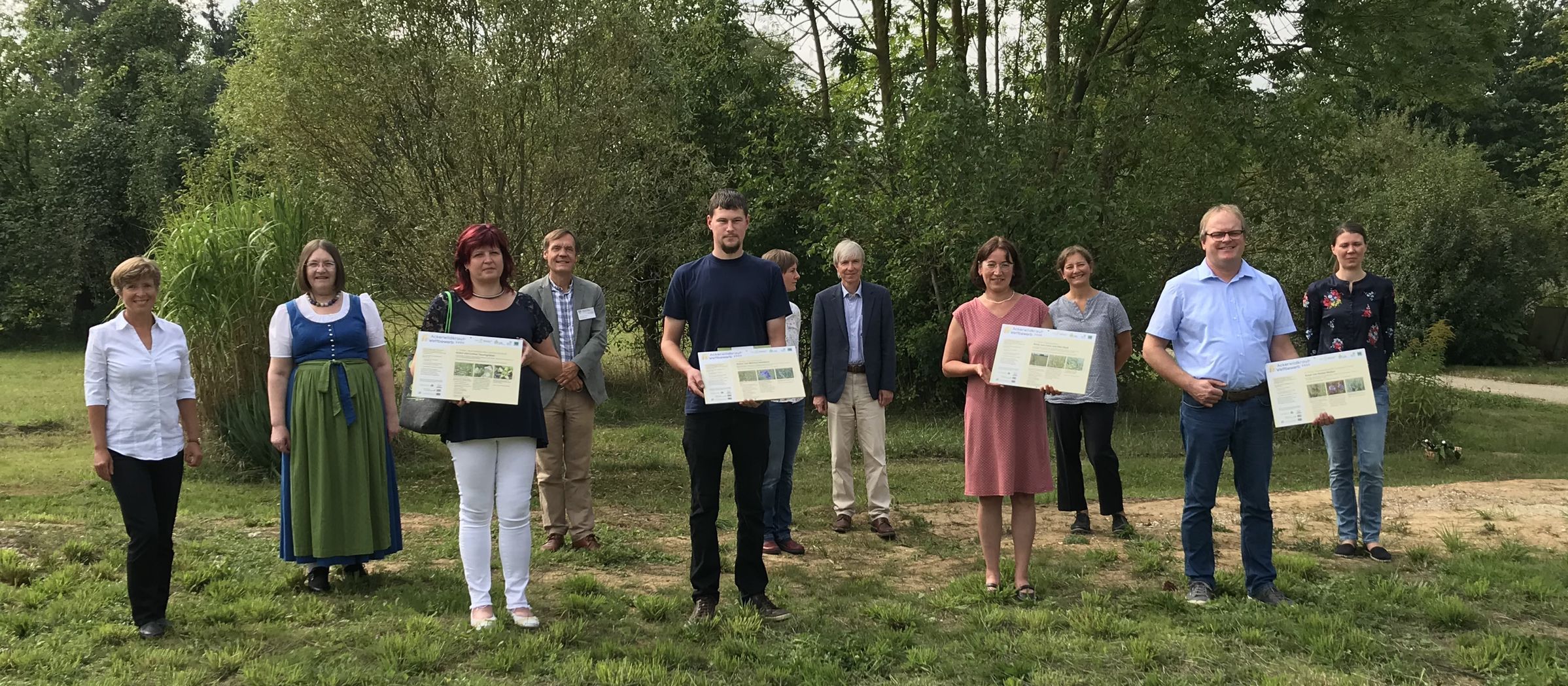 Eine Gruppe von Menschen steht mit Urkunden in der Hand auf einer Wiese. Die Preisträger des Ackerwildkraut-Wettbewerbs 2020. (Foto: Marion Ruppaner)