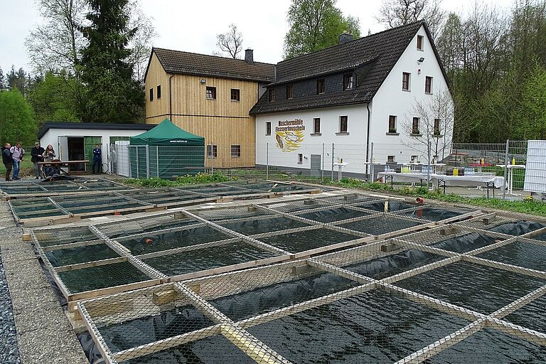 Ein saniertes altes Gebäude mit einem neuen Holzanbau und vielen Wasserbecken im Vordergrund