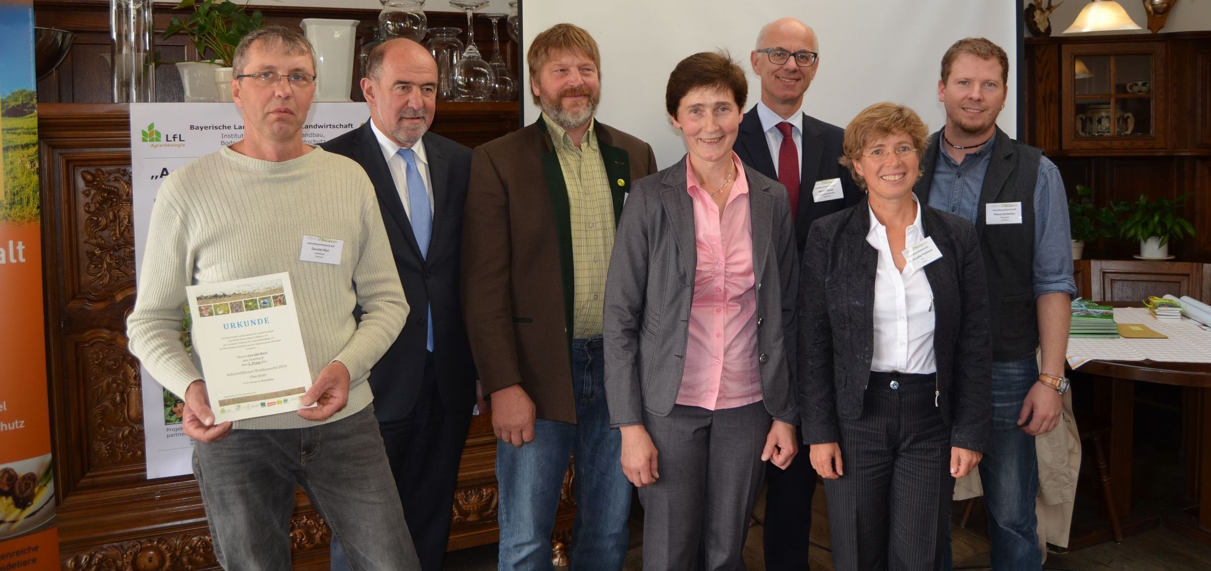 Preisverleihung 2016 Eine Gruppe von sechs Leuten steht in einem Saal. Einer hält eine Urkunde in den Händen. Die Preisverleihung für den Ackerwildkraut-Wettbewerb 2016 fand im September in Regensburg statt. (Tim Fluhrer/BN)